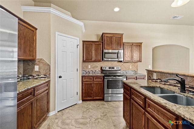 kitchen with decorative backsplash, appliances with stainless steel finishes, sink, and light stone counters