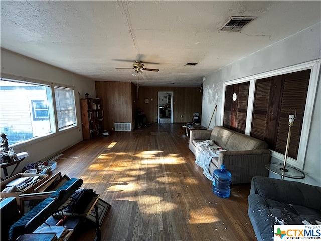 living room featuring a textured ceiling, dark wood-type flooring, wooden walls, and ceiling fan