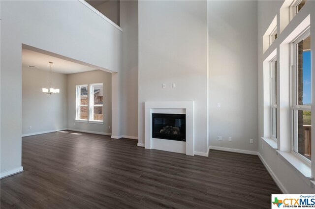 unfurnished living room with a high ceiling, dark hardwood / wood-style floors, and an inviting chandelier