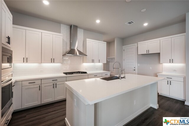 kitchen with white cabinets, wall chimney exhaust hood, sink, and an island with sink