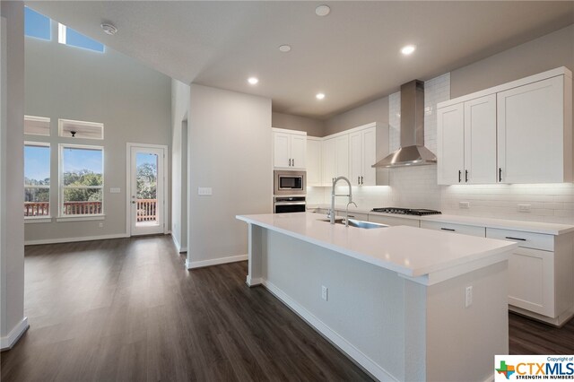 kitchen with sink, appliances with stainless steel finishes, wall chimney exhaust hood, an island with sink, and white cabinets