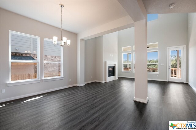 unfurnished living room with a notable chandelier, dark hardwood / wood-style floors, and lofted ceiling