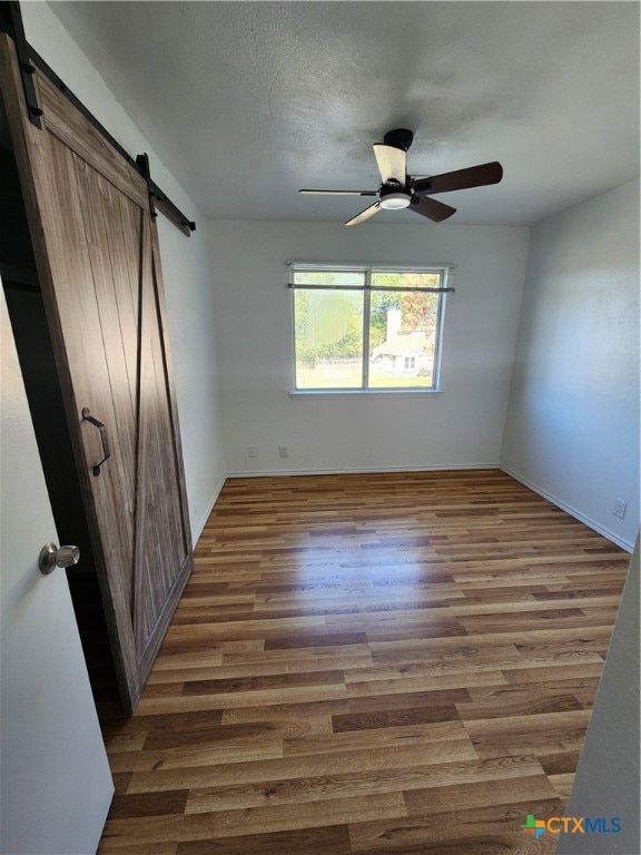 unfurnished bedroom with a barn door, dark hardwood / wood-style floors, a textured ceiling, and ceiling fan