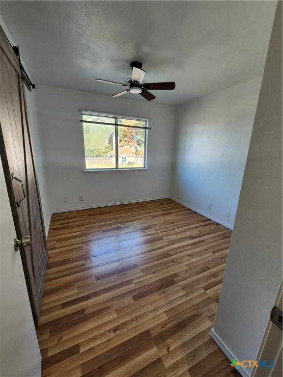 unfurnished room featuring a barn door, dark hardwood / wood-style floors, and ceiling fan