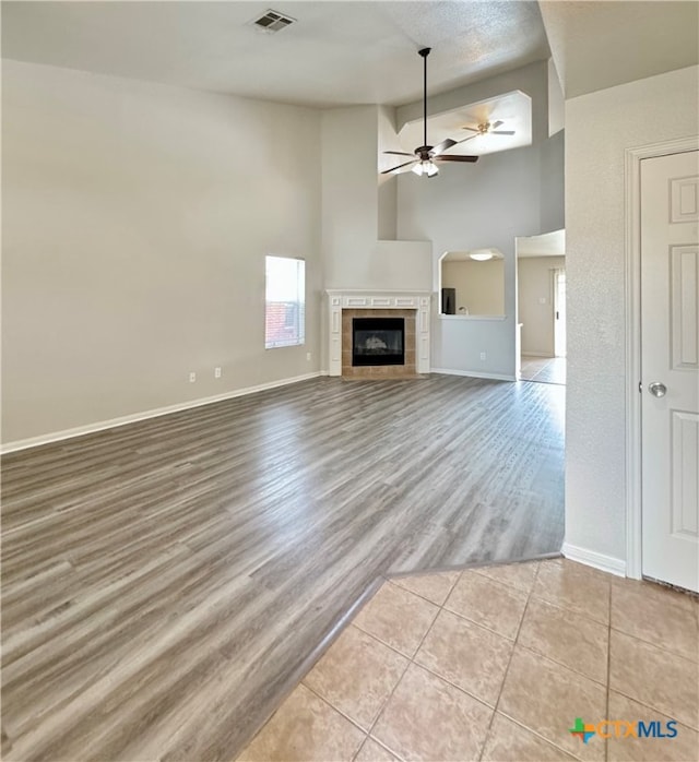 unfurnished living room with a fireplace, a high ceiling, ceiling fan, and light wood-type flooring