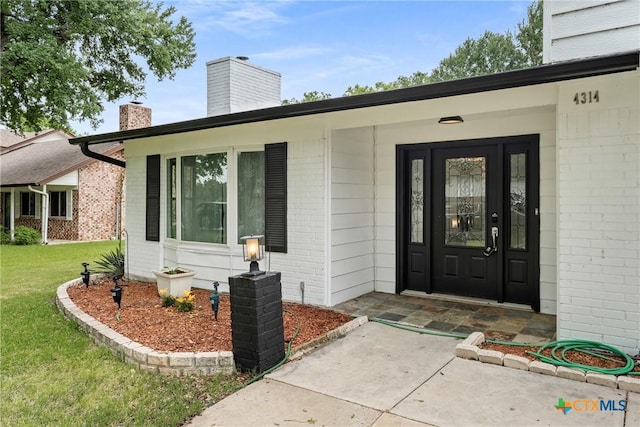 property entrance featuring a yard, a chimney, and brick siding