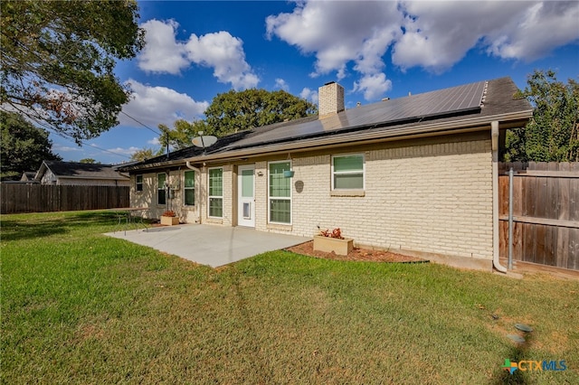 rear view of house featuring solar panels, a lawn, and a patio