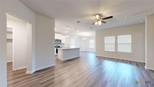 unfurnished living room with visible vents, ceiling fan with notable chandelier, baseboards, and wood finished floors