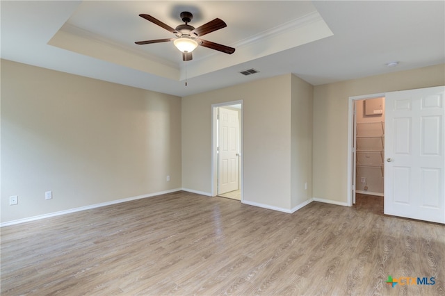 unfurnished bedroom featuring light hardwood / wood-style flooring, a spacious closet, ceiling fan, and a raised ceiling