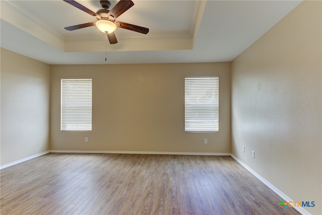 unfurnished room with ornamental molding, a wealth of natural light, a tray ceiling, and light hardwood / wood-style flooring