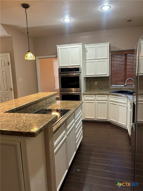 kitchen with stone counters, stainless steel double oven, hanging light fixtures, and sink