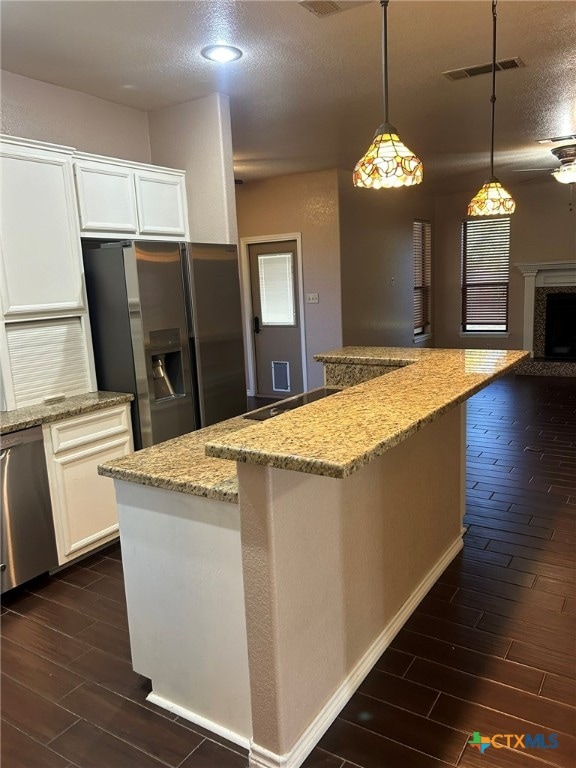 kitchen with stainless steel appliances, light stone countertops, white cabinets, and pendant lighting