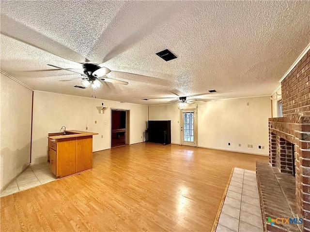 203 Hampshire St, Victoria, TX 77904 - unfurnished living room featuring a ceiling fan, light wood-style floors, a brick fireplace, a textured ceiling, and a sink