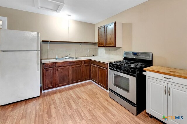 304 W Putnam, Ganado, TX 77962 - kitchen with freestanding refrigerator, gas range, a sink, light wood-style floors, and tasteful backsplash