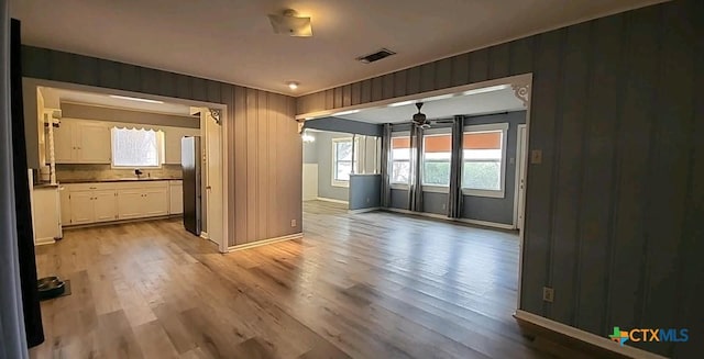 empty room with sink, light hardwood / wood-style flooring, and wood walls