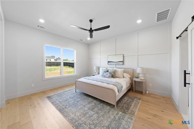 bedroom featuring a barn door, ceiling fan, and light hardwood / wood-style floors