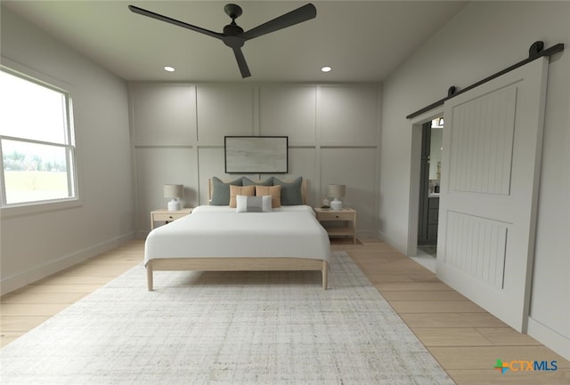 bedroom with light wood-type flooring, a barn door, and ceiling fan