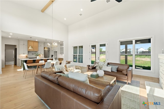 living room featuring high vaulted ceiling, ceiling fan with notable chandelier, light wood-type flooring, a fireplace, and beam ceiling