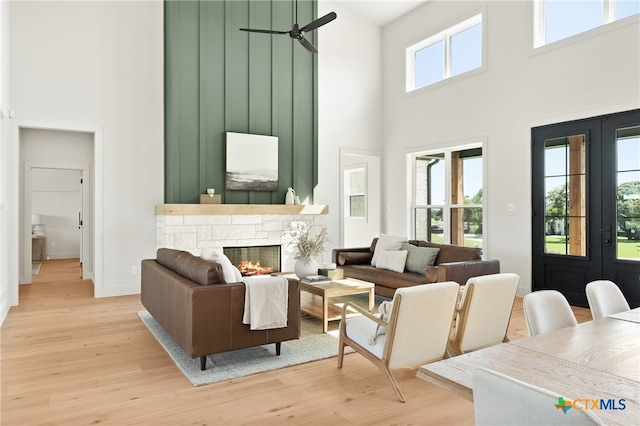 living room with ceiling fan, a towering ceiling, a healthy amount of sunlight, and light hardwood / wood-style floors