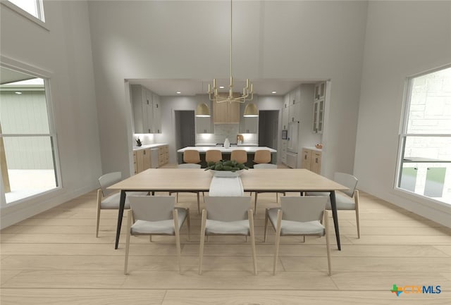 dining area with a towering ceiling, light hardwood / wood-style floors, and an inviting chandelier