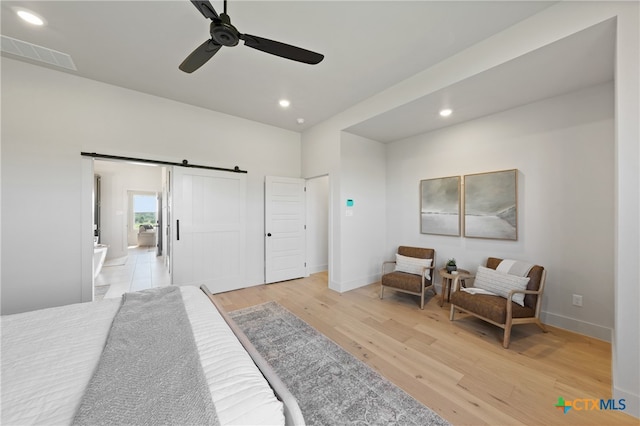 bedroom featuring a barn door, ceiling fan, and light hardwood / wood-style floors