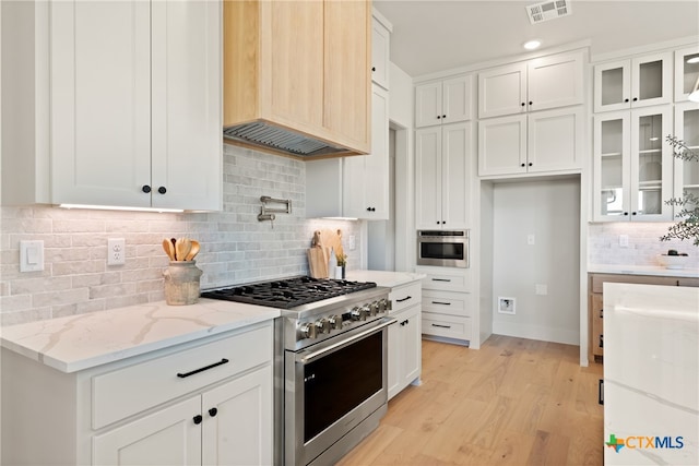 kitchen with backsplash, white cabinets, appliances with stainless steel finishes, light hardwood / wood-style floors, and light stone counters