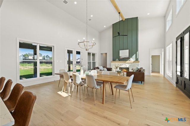 dining room with beam ceiling, french doors, a stone fireplace, light hardwood / wood-style flooring, and high vaulted ceiling