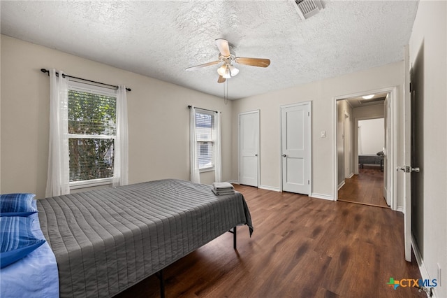 bedroom with dark wood-type flooring, ceiling fan, a textured ceiling, and multiple closets