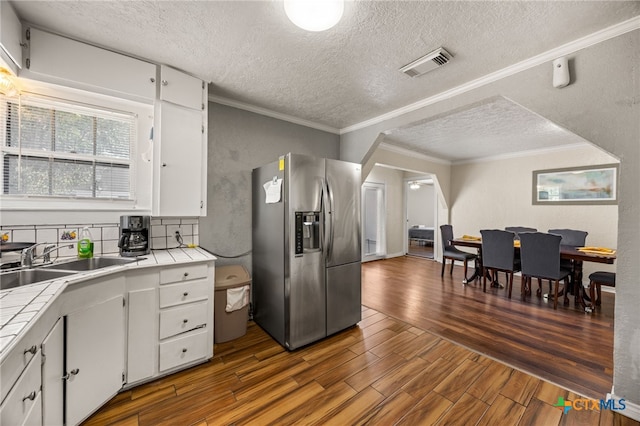 kitchen with tile counters, dark wood-type flooring, white cabinets, and stainless steel fridge