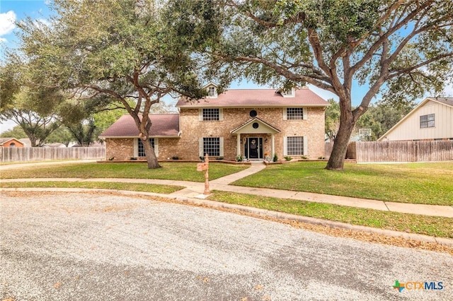 colonial-style house featuring brick siding, fence, and a front yard