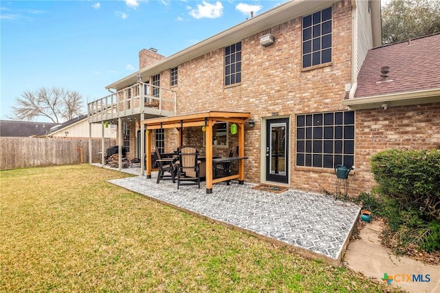 rear view of house featuring a lawn, a balcony, a chimney, fence, and brick siding