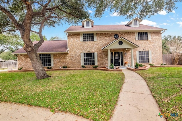 view of front of house featuring brick siding, fence, and a front yard