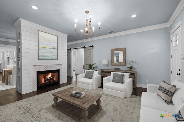 living room featuring a fireplace, crown molding, a barn door, hardwood / wood-style flooring, and a chandelier