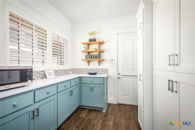 kitchen featuring blue cabinetry, stainless steel microwave, open shelves, and dark wood-style floors
