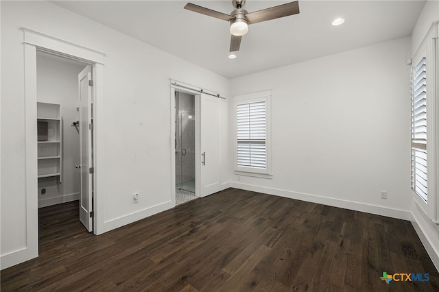 unfurnished bedroom featuring a barn door, a spacious closet, ceiling fan, and dark wood-type flooring