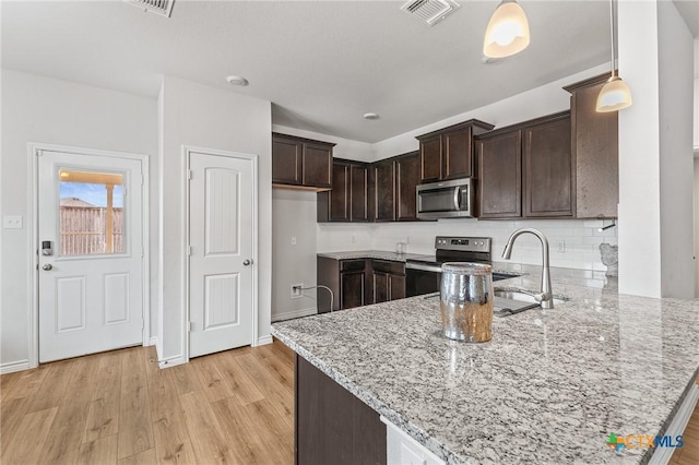 5836 Copano Rd, Belton, TX 76513 - kitchen featuring appliances with stainless steel finishes, a peninsula, dark brown cabinetry, light stone counters, and light wood-style floors