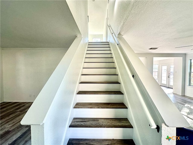 staircase with a textured ceiling, french doors, and hardwood / wood-style flooring