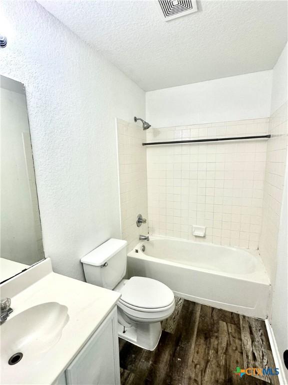 full bathroom with hardwood / wood-style floors, toilet, vanity, tiled shower / bath, and a textured ceiling