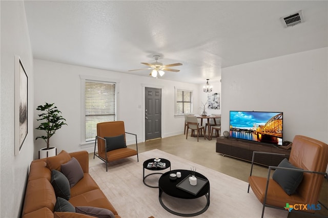 carpeted living area with ceiling fan with notable chandelier, visible vents, a wealth of natural light, and baseboards