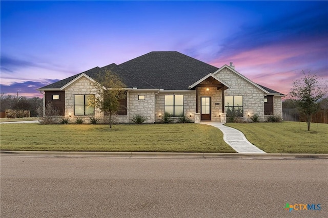 view of front of home featuring stone siding, a shingled roof, and a lawn