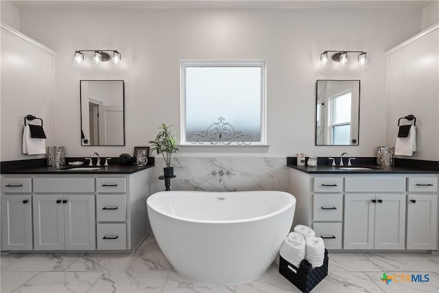 full bath with marble finish floor, a freestanding tub, two vanities, and a sink