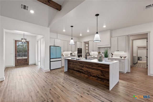 kitchen featuring visible vents, stainless steel double oven, a sink, and freestanding refrigerator