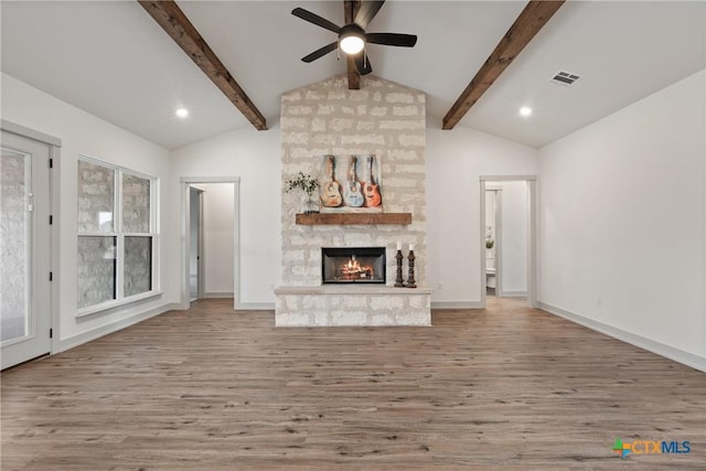 unfurnished living room featuring vaulted ceiling with beams, a stone fireplace, wood finished floors, and visible vents