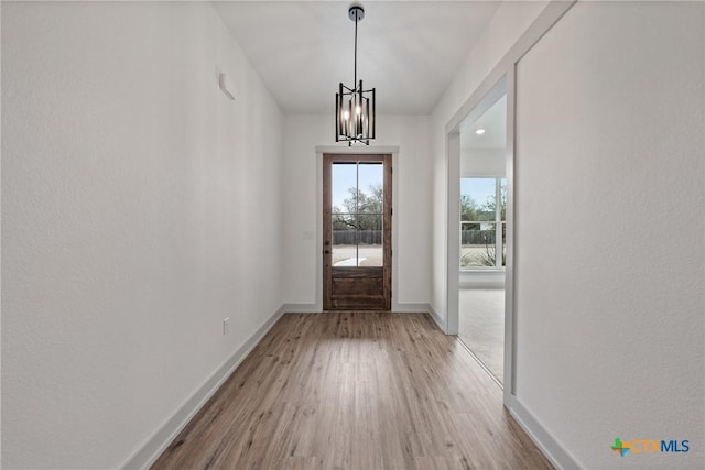 doorway to outside with baseboards, a chandelier, and wood finished floors