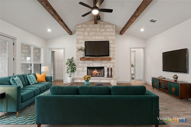 living area with a fireplace, visible vents, lofted ceiling with beams, wood finished floors, and baseboards