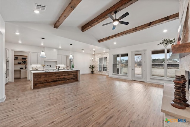 living area featuring vaulted ceiling with beams, ceiling fan, light wood-style flooring, a large fireplace, and visible vents