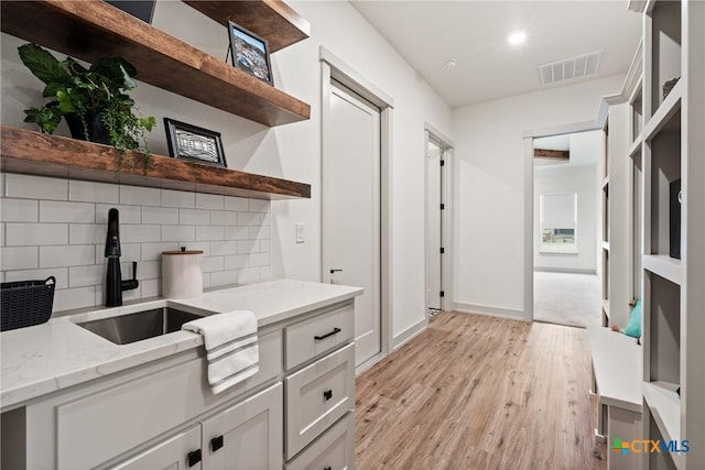 interior space featuring a sink, visible vents, light wood-type flooring, open shelves, and tasteful backsplash