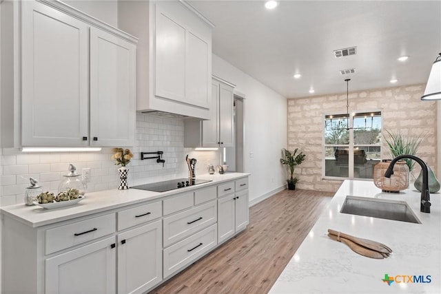 kitchen featuring tasteful backsplash, visible vents, black electric cooktop, light wood-style floors, and a sink