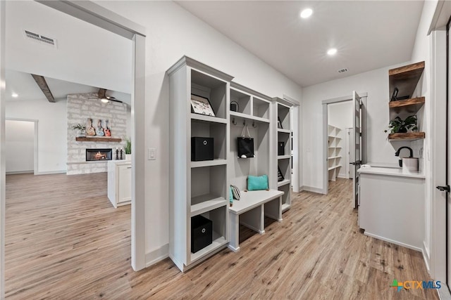 mudroom with beam ceiling, light wood finished floors, visible vents, a ceiling fan, and a stone fireplace