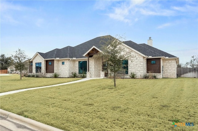 view of front of house with a shingled roof, stone siding, a chimney, fence, and a front yard